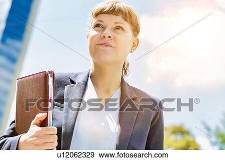 Stock Photo - Portrait of young beautiful businesswoman standing while holding documents. Fotosearch