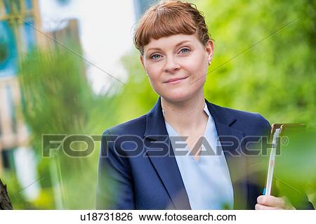Stock Photograph - Portrait of young beautiful businesswoman standing while holding documents. Fotosearch