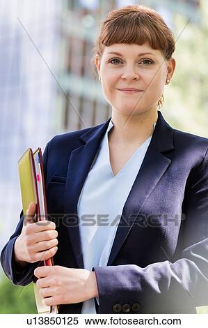 Stock Photography - Portrait of young beautiful businesswoman standing while holding documents. Fotosearch