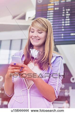 Picture - Portrait of young beautiful teenage girl using smartphone in airport with lens flare. Fotosearch