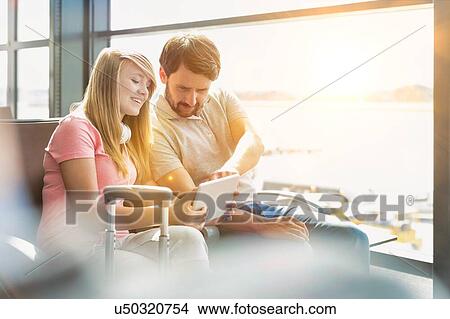 Picture - Portrait of young beautiful teenage girl showing digital tablet to her father while sitting and waiting for their flight in airport. Fotosearch