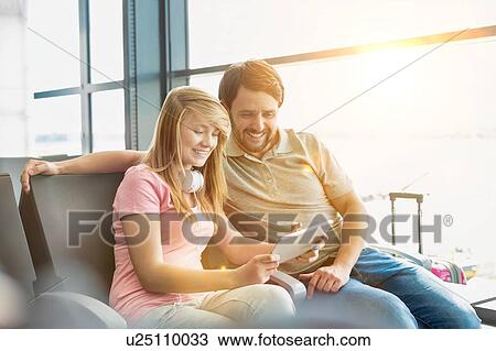 Portrait of young beautiful teenage girl showing digital tablet to her father while sitting and waiting for their flight in airport View Large Photo Image Stock Image - Portrait of young beautiful teenage girl showing digital tablet to her father while sitting and waiting for their flight in airport. Fotosearch