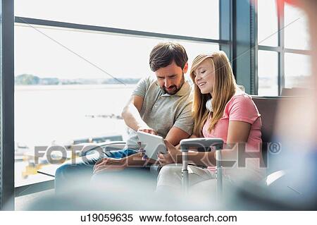 Portrait of young beautiful teenage girl showing digital tablet to her father while sitting and waiting for their flight in airport View Large Photo Image Stock Photography - Portrait of young beautiful teenage girl showing digital tablet to her father while sitting and waiting for their flight in airport. Fotosearch