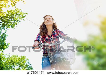 Picture - Portrait of young beautiful woman smiling while riding bicycle in the middle of the city. Fotosearch