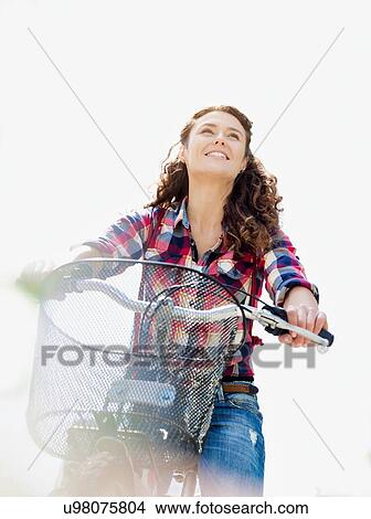 Portrait of young beautiful woman smiling while riding bicycle in the middle of the city with lens flare in background View Large Photo Image Picture - Portrait of young beautiful woman smiling while riding bicycle in the middle of the city with lens flare in background. Fotosearch