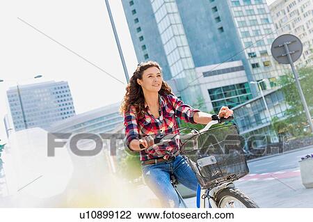 Stock Image - Portrait of young beautiful woman smiling while riding bicycle in the middle of the city. Fotosearch
