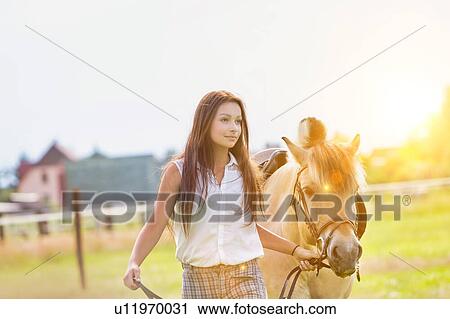 Stock Image - Portrait of young beautiful woman standing with horse in ranch. Fotosearch