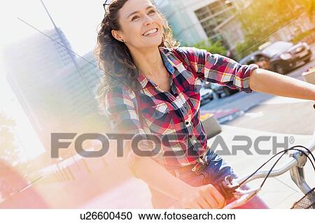 Portrait of young beautiful woman smiling while riding bicycle in the middle of the city View Large Photo Image Stock Image - Portrait of young beautiful woman smiling while riding bicycle in the middle of the city. Fotosearch
