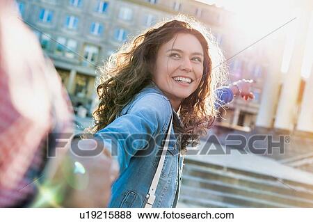 Stock Photo - Portrait of young beautiful woman smiling and walking while holding her boyfriend hand . Fotosearch