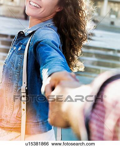 Stock Photograph - Portrait of young beautiful woman posing while being photograph by his boyfriend with lens flare in background. Fotosearch