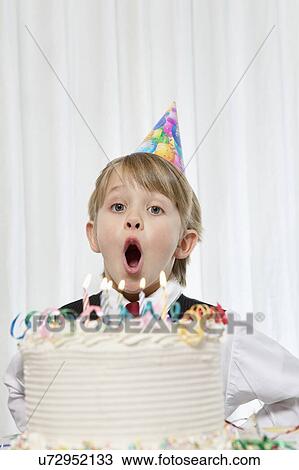 Portrait of young boy wearing party hat blowing candles on birthday cake View Large Photo Image Stock Image - Portrait of young boy wearing party hat blowing candles on birthday cake. Fotosearch