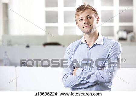Picture - Portrait of young businessman with arms crossed standing at office. Fotosearch