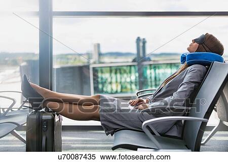 Stock Photography - Portrait of young businesswoman sleeping with her head pillow and eye mask while waiting for boarding in airport. Fotosearch
