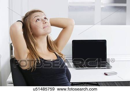 Portrait of young businesswoman with hands behind head sitting in front of desk in office View Large Photo Image Stock Photo - Portrait of young businesswoman with hands behind head sitting in front of desk in office. Fotosearch