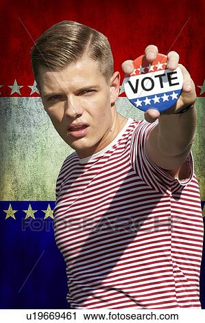 Stock Image - Portrait of young Caucasian man displaying vote badge standing outdoors. Fotosearch