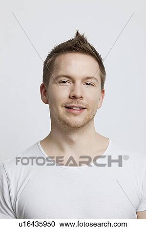 Stock Image - Portrait of young Caucasian man with spiked hair against white background. Fotosearch