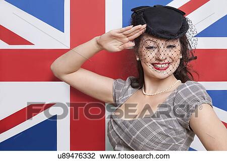 Stock Image - Portrait of young Caucasian woman with veiled hat saluting against British flag. Fotosearch