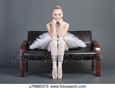 Stock Image - Portrait of young female ballet dancer sitting on sofa over grey background. Fotosearch