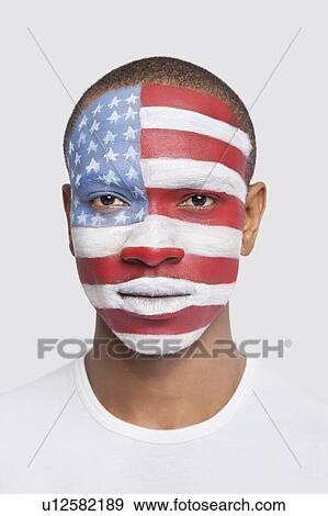 Stock Photo - Portrait of young Hispanic man with North American flag painted on face against white background. Fotosearch