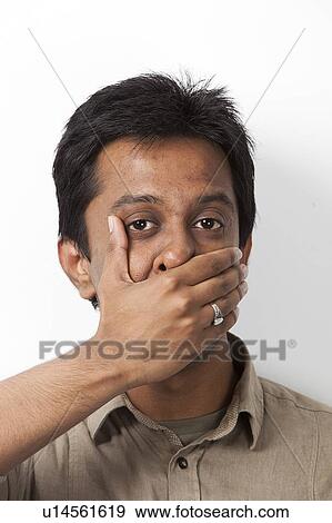 Portrait of young Indian man covering his mouth against white background View Large Photo Image Stock Photo - Portrait of young Indian man covering his mouth against white background. Fotosearch