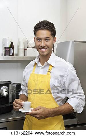Picture - Portrait of young male waiter holding cup and saucer. Fotosearch