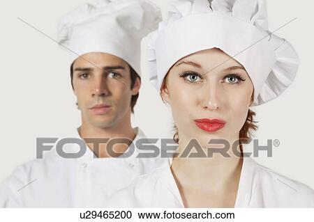 Stock Image - Portrait of young man and woman in chef's uniform against gray background. Fotosearch