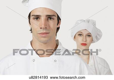 Stock Image - Portrait of young man and woman in chef's uniform against gray background. Fotosearch