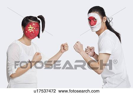 Stock Image - Portrait of young man and woman with Asian flags painted on face holding up their fists to fight against white background. Fotosearch