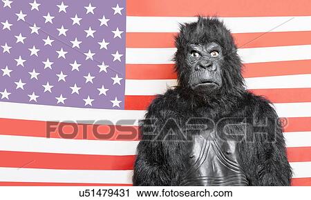 Stock Image - Portrait of young man dressed up in gorilla costume against American flag. Fotosearch