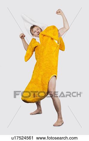 Stock Image - Portrait of young man in banana costume flexing muscle against gray background. Fotosearch