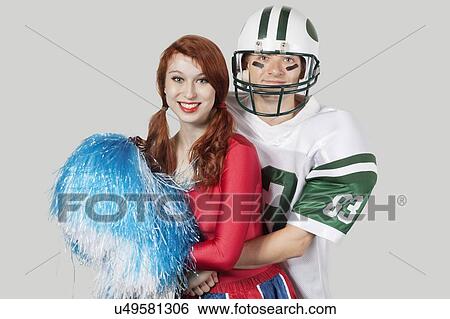 Portrait of young man in football uniform hugging cheerleader over gray background View Large Photo Image Stock Photograph - Portrait of young man in football uniform hugging cheerleader over gray background. Fotosearch