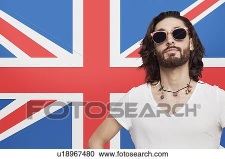 Stock Image - Portrait of young man in white t-shirt wearing sunglasses against British flag. Fotosearch