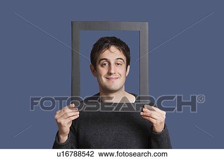 Portrait of young man smiling through frame over blue background View Large Photo Image Stock Image - Portrait of young man smiling through frame over blue background. Fotosearch