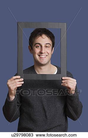 Portrait of young man smiling through frame over blue background View Large Photo Image Stock Image - Portrait of young man smiling through frame over blue background. Fotosearch