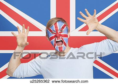 Stock Image - Portrait of young man with face painting screaming against British flag. Fotosearch