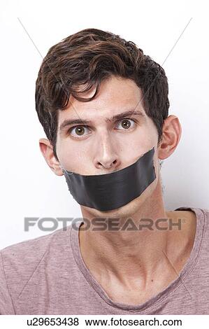 Stock Photo - Portrait of young man with tape over his mouth staring over white background. Fotosearch