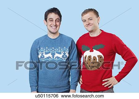 Stock Photograph - Portrait of young men in warm clothing standing against blue background. Fotosearch