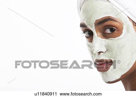 Stock Image - Portrait of young Mixed Race woman with face pack against white background. Fotosearch