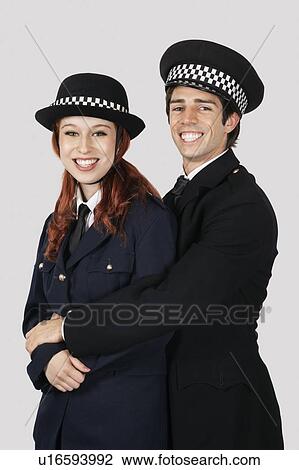 Stock Image - Portrait of young police officers embracing against gray background. Fotosearch