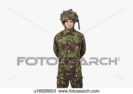Stock Image - Portrait of young soldier standing against gray background. Fotosearch