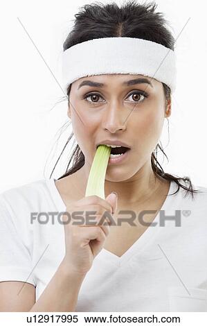 Stock Photography - Portrait of young sportswoman eating celery over white background. Fotosearch