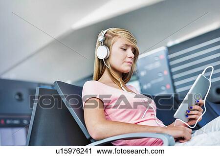 Portrait of young teenage girl sitting while watching movie on her digital tablet with headphones on in airport View Large Photo Image Stock Image - Portrait of young teenage girl sitting while watching movie on her digital tablet with headphones on in airport. Fotosearch