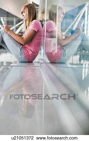 Stock Image - Portrait of young teenage girl sitting on the floor and using digital tablet while waiting for her flight in airport. Fotosearch