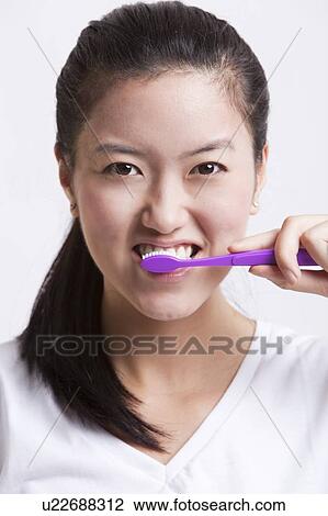 Stock Image - Portrait of young woman brushing her teeth against white background. Fotosearch