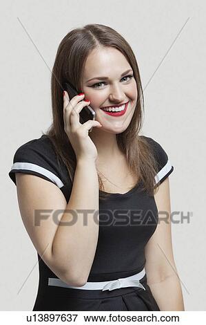 Stock Photo - Portrait of young woman communicating on cell phone over gray background. Fotosearch