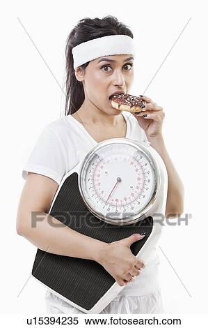 Portrait of young woman eating donut holding weight scale over white background View Large Photo Image Stock Photography - Portrait of young woman eating donut holding weight scale over white background. Fotosearch
