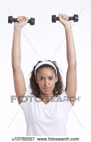 Stock Photo - Portrait of young woman exercising with dumbbells against white background. Fotosearch