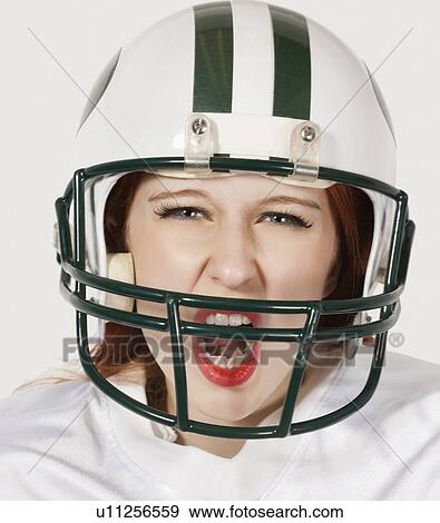 Stock Photo - Portrait of young woman in football uniform screaming against gray background. Fotosearch