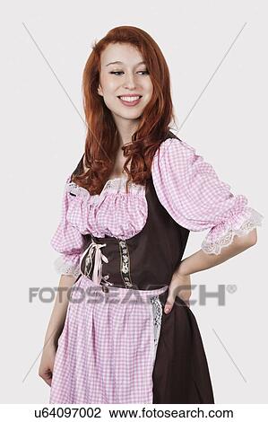 Stock Image - Portrait of young woman in maid costume standing against gray background. Fotosearch