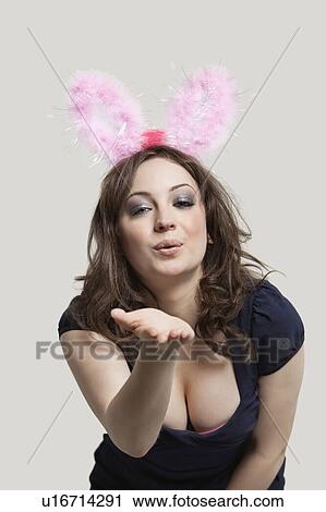 Stock Image - Portrait of young woman in playboy bunny costume blowing kiss over gray background. Fotosearch
